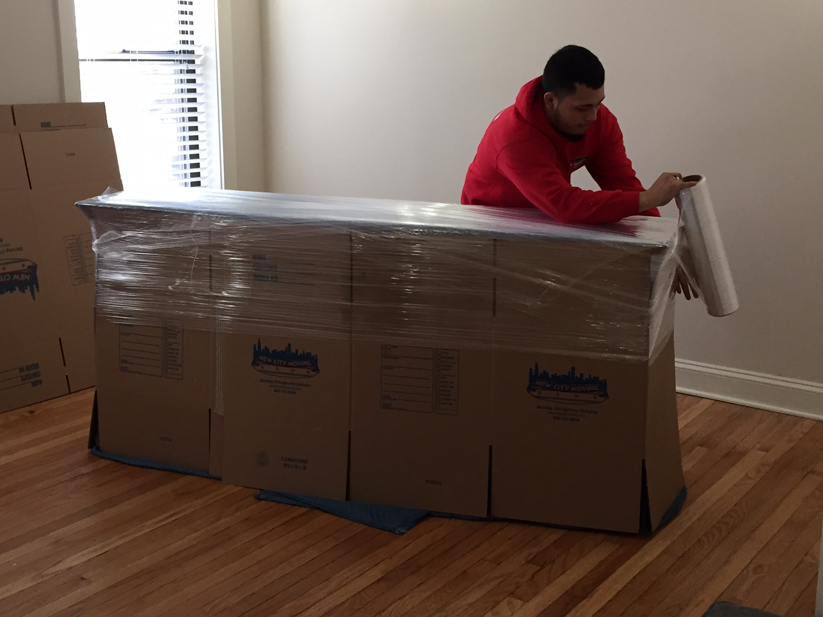 New city moving employee wrapping cardboard boxes with wrapping paper.